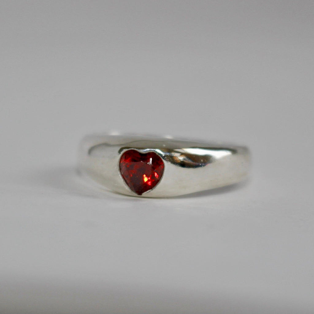 Silver ring with a heart-shaped red gemstone on a gray background