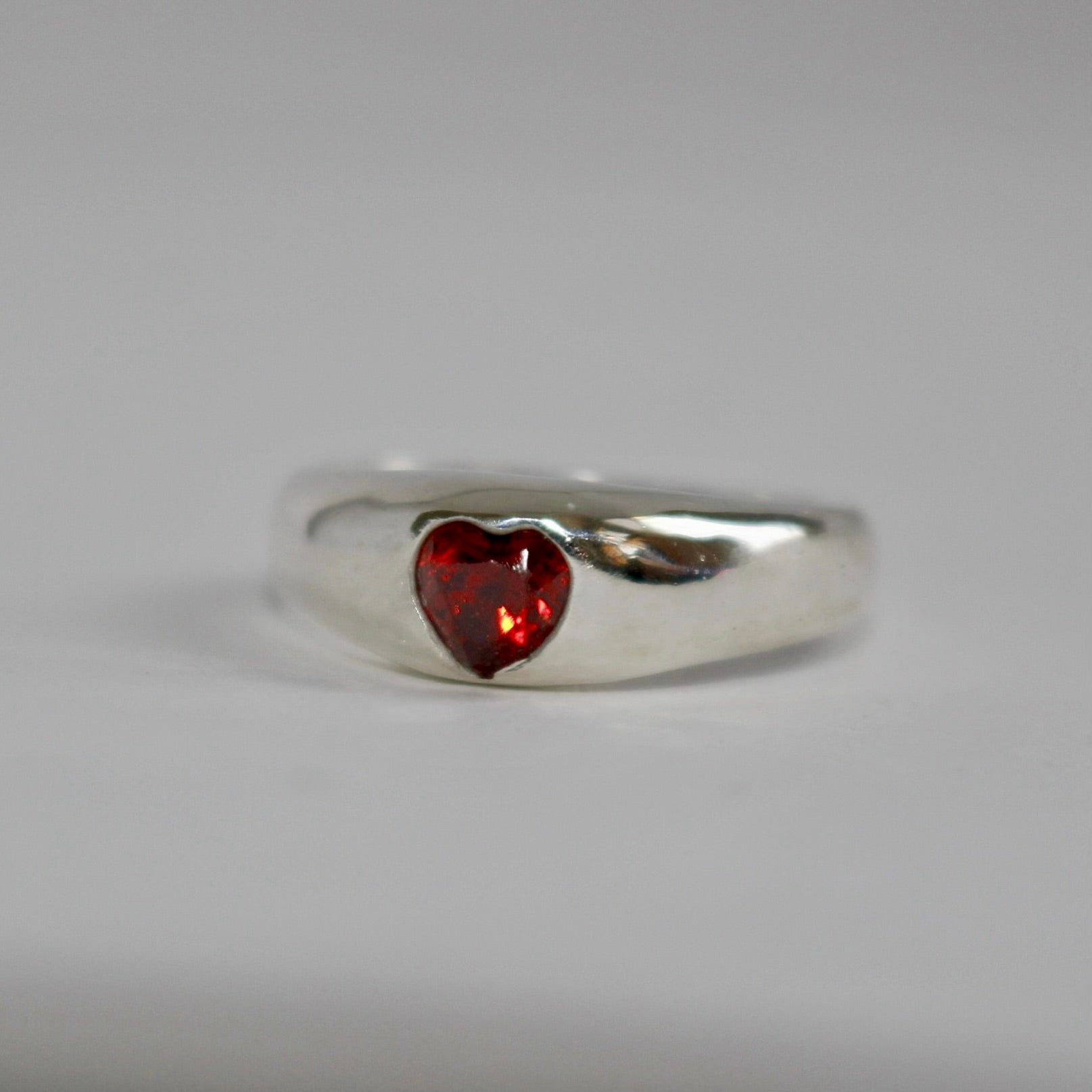 Silver ring with a heart-shaped red gemstone on a gray background