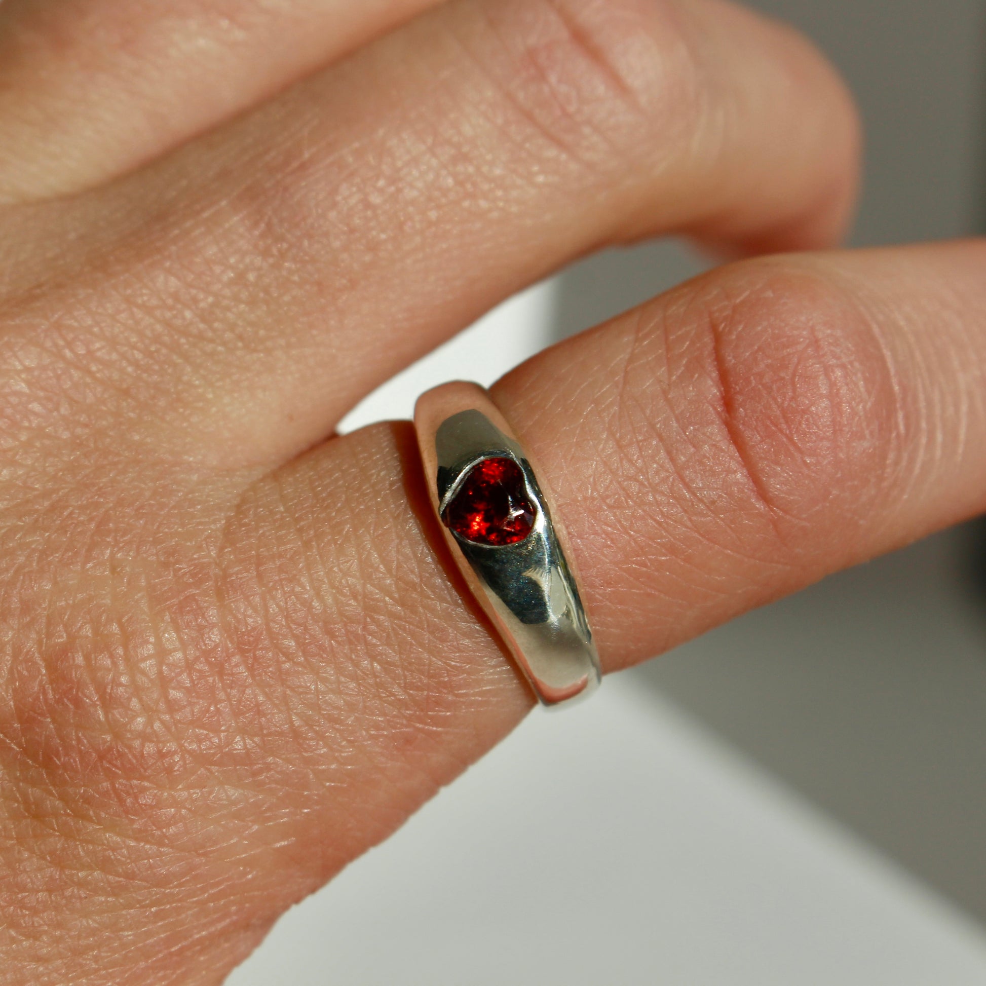 Silver ring with a red gemstone on a finger against a neutral background
