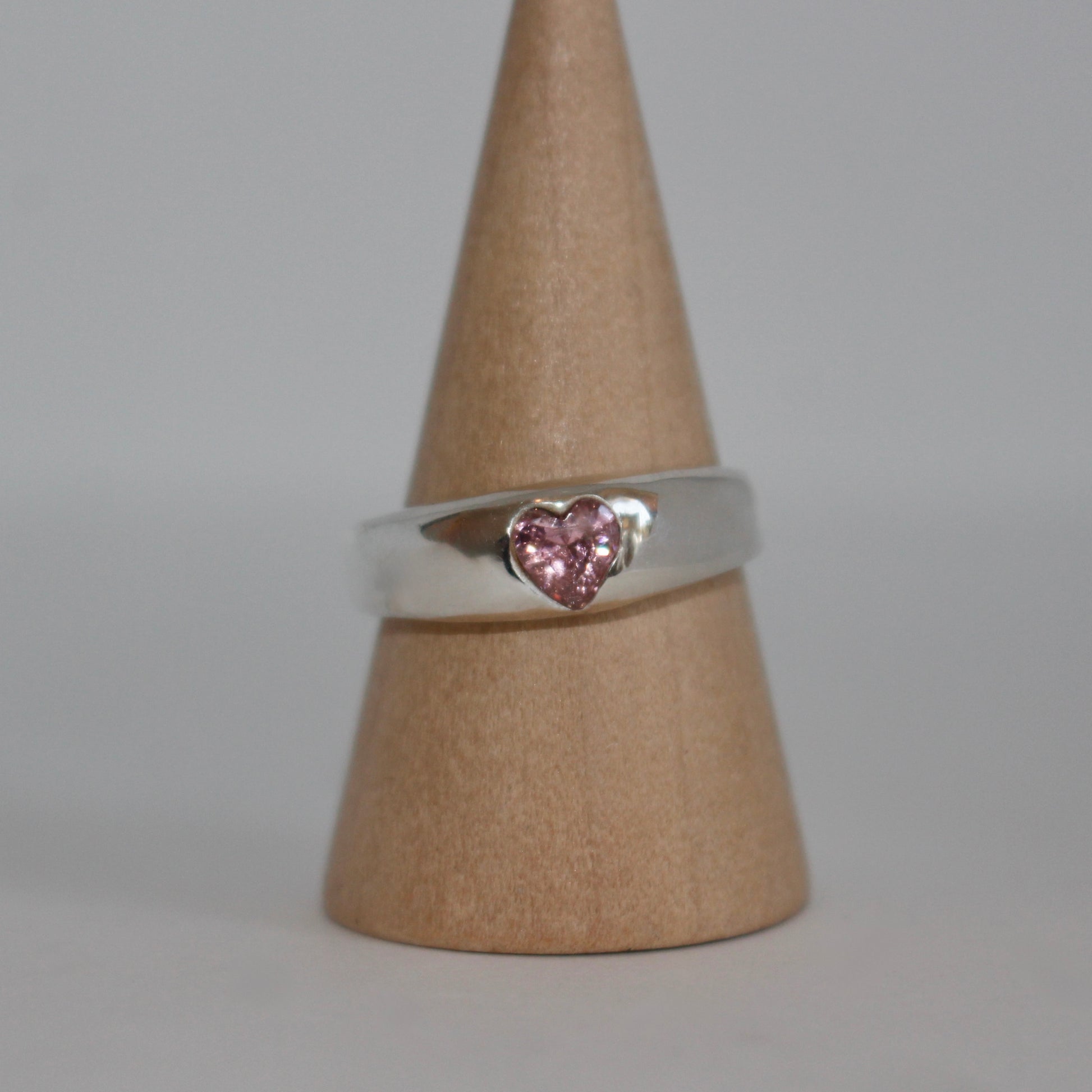 Silver ring with a pink heart-shaped gemstone on a brown cone against a gray background
