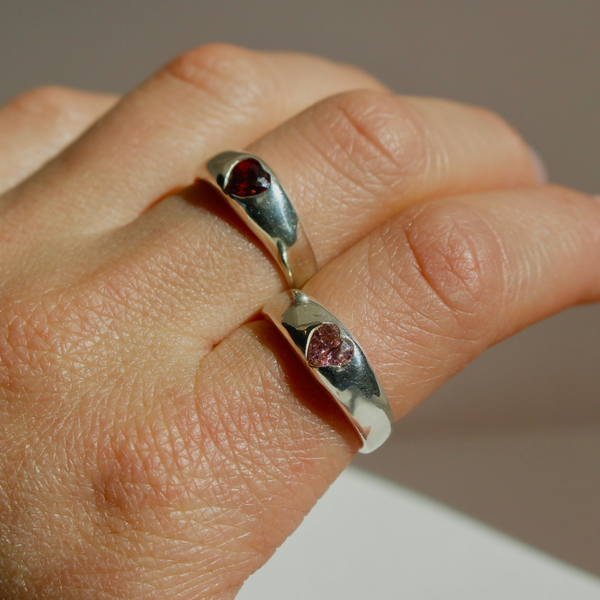 Silver ring with red gemstones on a person's finger against a neutral background